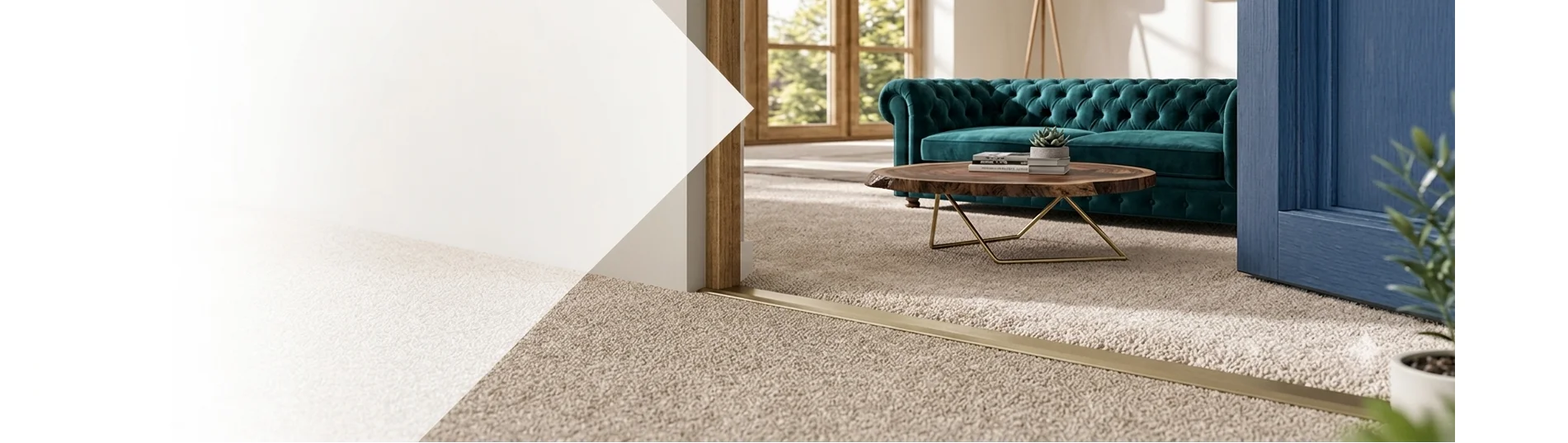 Sleek brass carpet-to-carpet door threshold strip installed under a doorway, connecting two rooms with beige carpeting and leading into a modern living room with a teal velvet sofa.